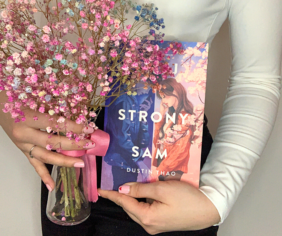 zdjęcie przedstawia książkę Z tej strony Sam, którą trzyma kobieta z kwiatami